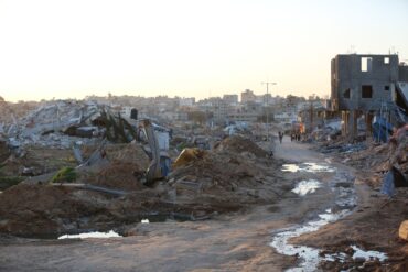 Menschen gehen an Trümmern und Ruinen auf einer Straße im Flüchtlingslager Al-Maghazi im Zentrum des Gazastreifens vorbei.