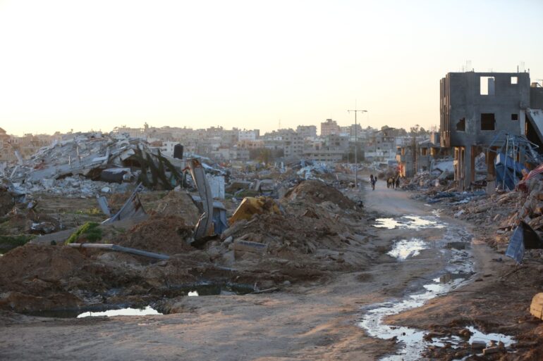 Menschen gehen an Trümmern und Ruinen auf einer Straße im Flüchtlingslager Al-Maghazi im Zentrum des Gazastreifens vorbei.