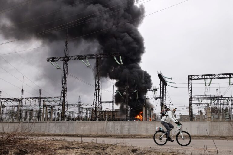 Nach einem russischen Angriff fährt ein Mann mit seinem Rad an einem brennenden Elektrizitätswerk in Charkiw vorbei.