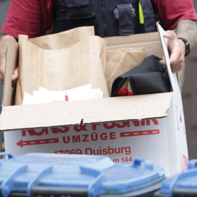 Ein Polizist trägt nach einer Wohnungsdurchsuchung einen Karton mit sichergestellten Gegenständen.