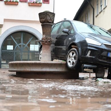 Auf einem Brunnen in Rudersberg hängt ein durch das Hochwasser weggespültes Auto.