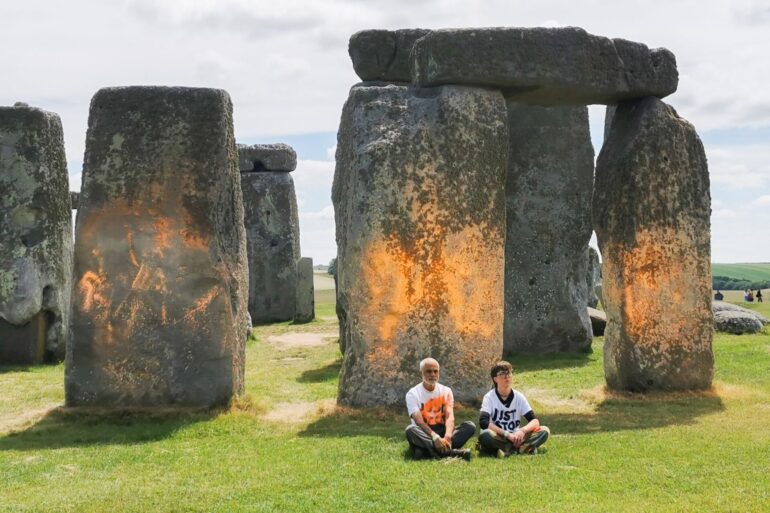 Demonstranten von «Just Stop Oil» sitzen vor dem Steinmonument Stonehenge, das sie zuvor mit orangener Farbe besprüht haben.