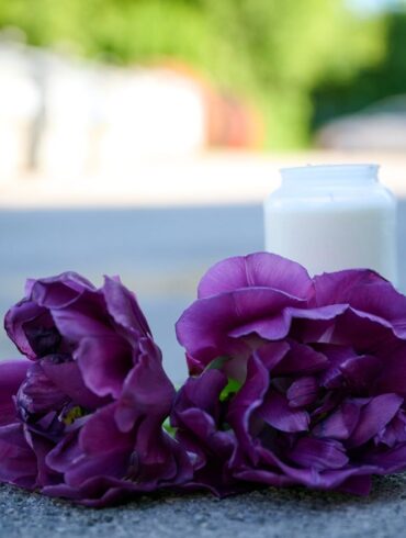 Blumen und eine Kerze liegen auf einem Schotterplatz vor dem Eingang zum Spielplatz, auf dem in der Nacht ein 17-Jähriger einen 14-Jährigen erstochen haben soll.