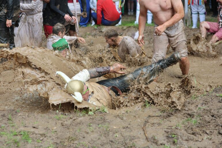 Teilnehmer springen auf dem Dreckschweinfest 2025 auf dem Festivalgelände auf der Wildbahn in ein Schlammloch.