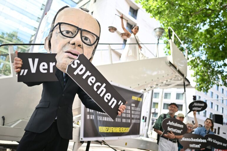 Ein Aktivist mit Merz-Maske zerbricht während einer symbolischen Protestaktion von Kabul Luftbrücke und Campact ein Schild mit der Aufschrift «Versprechen».