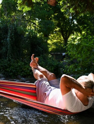 Ein Mann schaukelt im Berliner in einer Hängematte über dem Wasser.