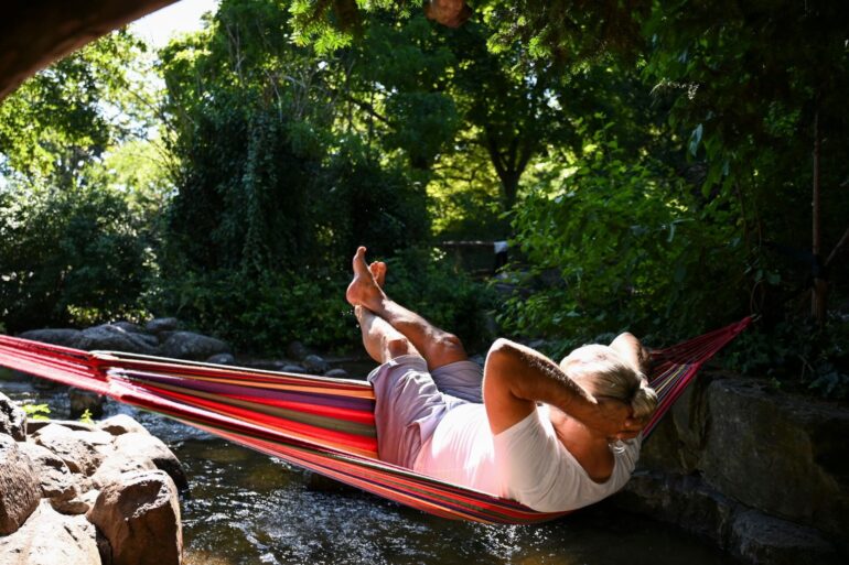 Ein Mann schaukelt im Berliner in einer Hängematte über dem Wasser.