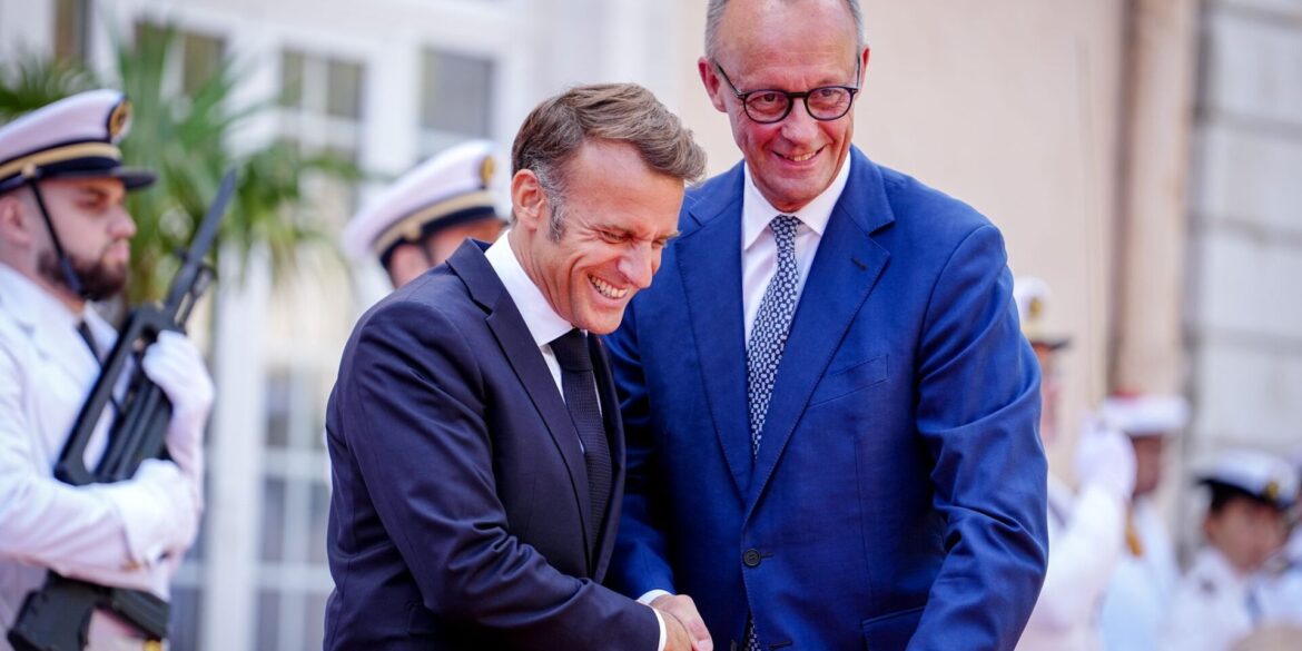 Wie zwei alte Freunde begrüßen sich Macron und Merz vor dem Fort du Cap Brun über der Cote d'Azur.