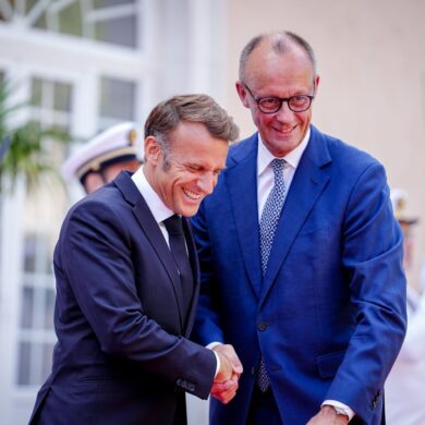 Wie zwei alte Freunde begrüßen sich Macron und Merz vor dem Fort du Cap Brun über der Cote d'Azur.