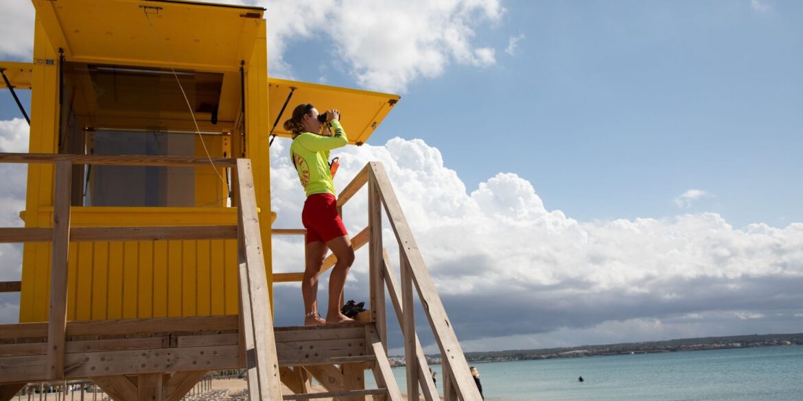 Ein Rettungsschwimmer benutzt ein Fernglas, während er am Strand von Palma auf Mallorca patrouilliert.