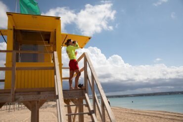Ein Rettungsschwimmer benutzt ein Fernglas, während er am Strand von Palma auf Mallorca patrouilliert.