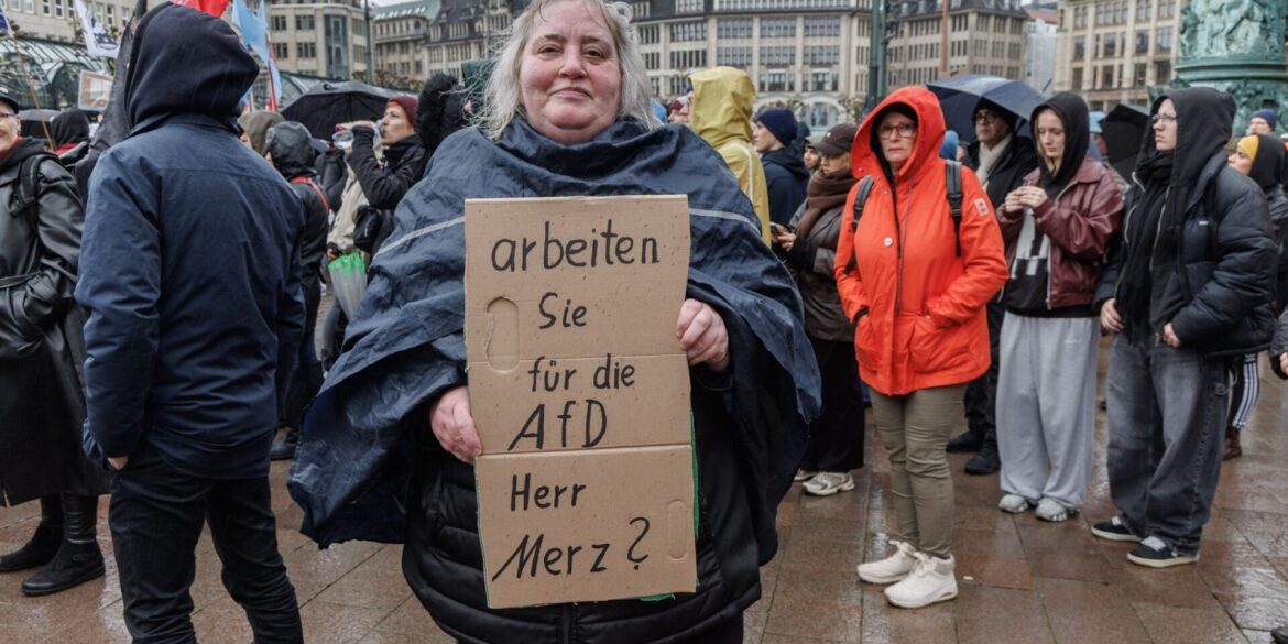 Eine Demonstrantin in Hamburg stellt auf einem Pappschild eine Frage an Bundeskanzler Friedrich Merz (CDU).