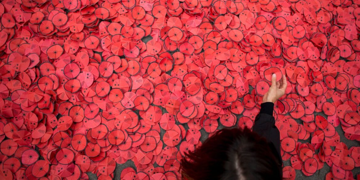 Eine Person hebt eine Papiermohnblume auf, die während einer Kundgebung gegen den Gaza-Krieg vor dem spanischen Außenministerium in Madrid auf dem Boden liegt.