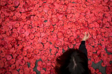 Eine Person hebt eine Papiermohnblume auf, die während einer Kundgebung gegen den Gaza-Krieg vor dem spanischen Außenministerium in Madrid auf dem Boden liegt.