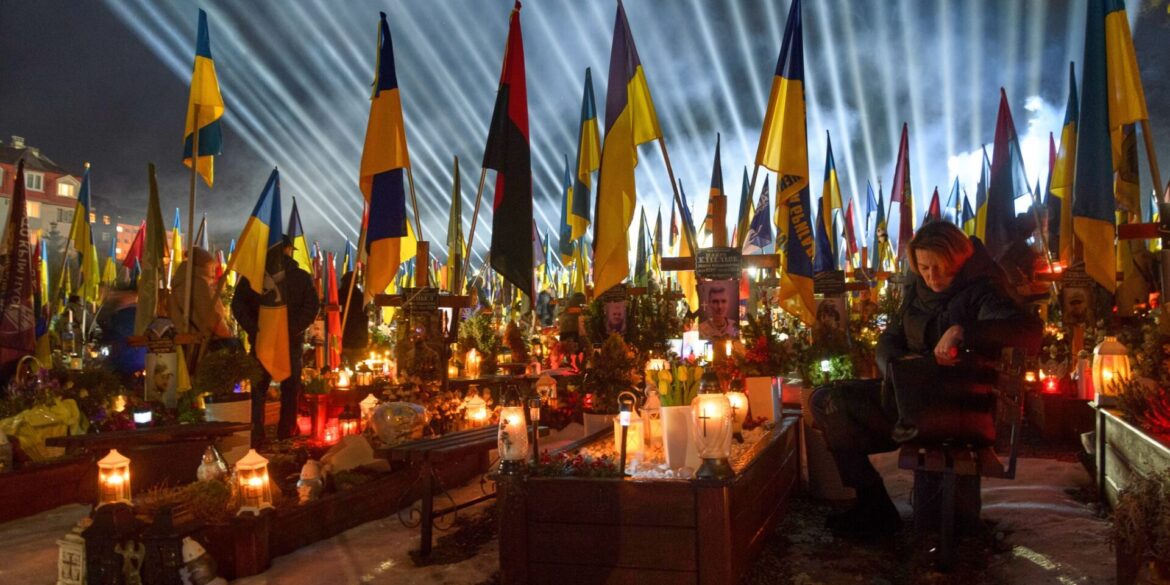 Flutlichter leuchten in Lwiw über den Gräbern der gefallener Soldaten, während Menschen am Vorabend des vierten Jahrestages der russischen Invasion Kerzen anzünden.