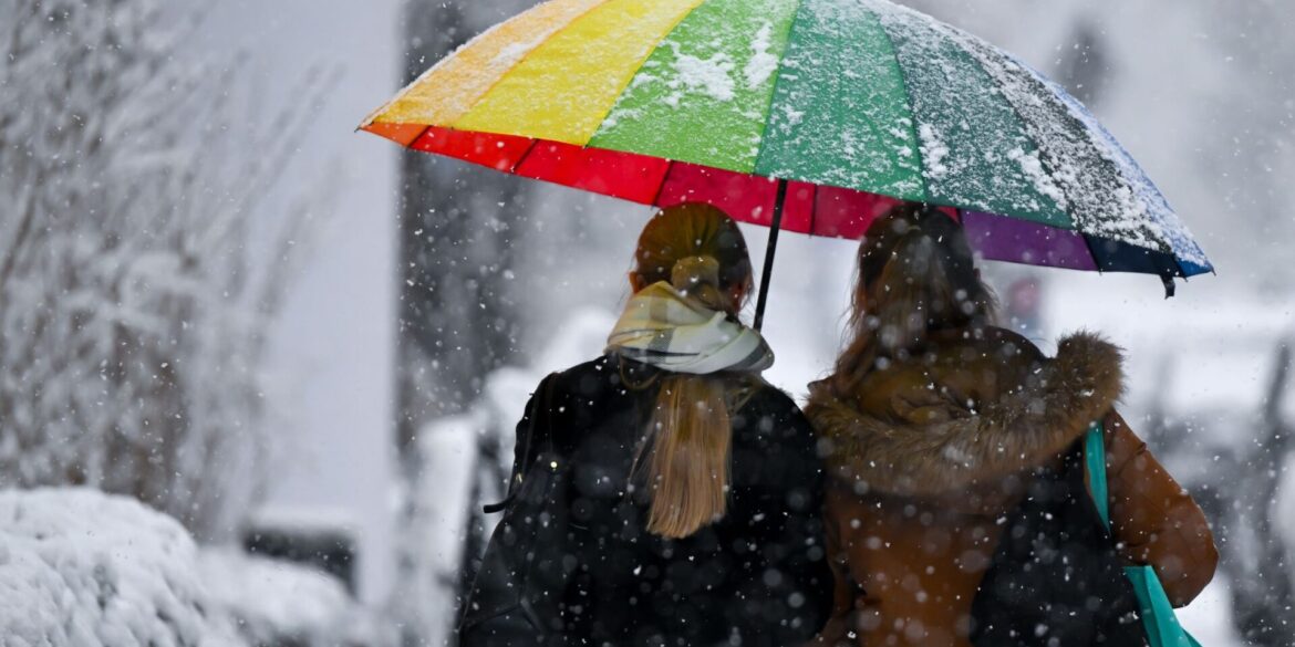 Bunt und grau zugleich: Zwei Frauen gehen mit einem Schirm bei Schneefall in München.
