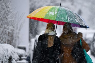 Bunt und grau zugleich: Zwei Frauen gehen mit einem Schirm bei Schneefall in München.