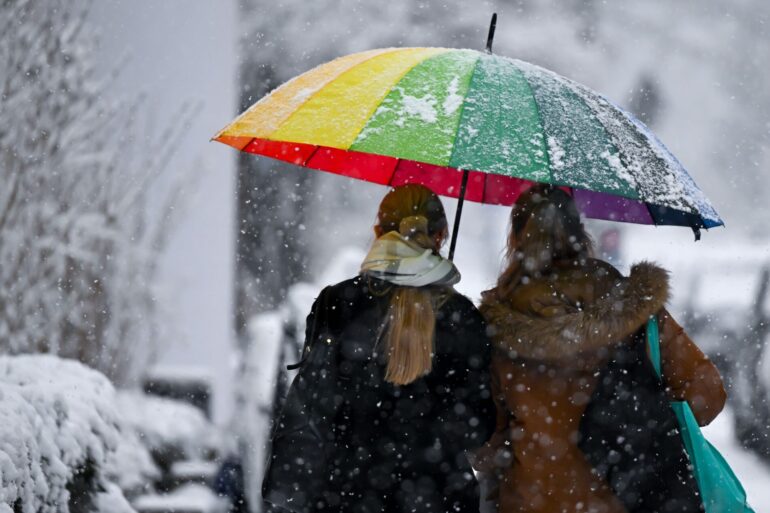 Bunt und grau zugleich: Zwei Frauen gehen mit einem Schirm bei Schneefall in München.