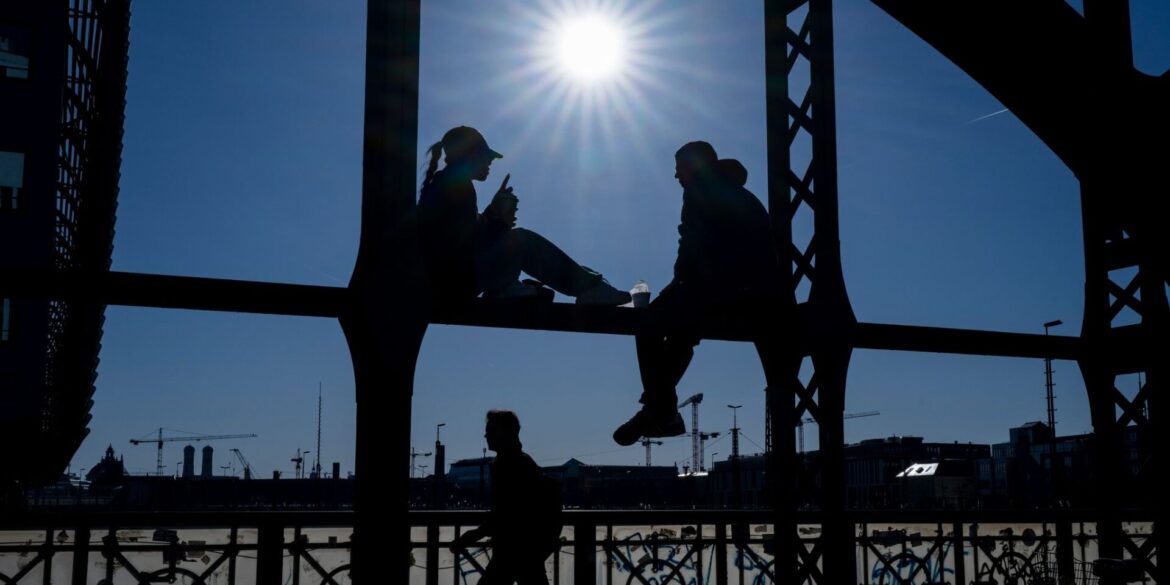 Ein Pärchen sitzt in der Sonne auf dem Geländer der Hackerbrücke in München.