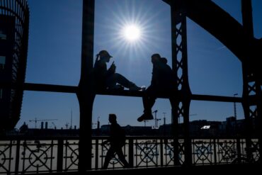 Ein Pärchen sitzt in der Sonne auf dem Geländer der Hackerbrücke in München.
