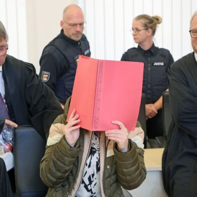 Die Angeklagte sitzt mit Aktendeckel vor dem Gesicht zwischen ihren Verteidigern Andreas Ohm (l-r) und Thomas Löcker.