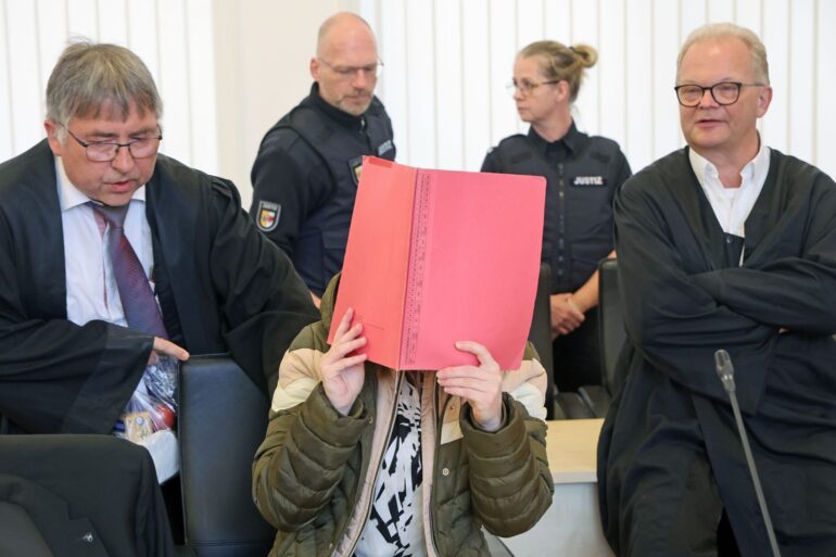 Die Angeklagte sitzt mit Aktendeckel vor dem Gesicht zwischen ihren Verteidigern Andreas Ohm (l-r) und Thomas Löcker.