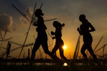Menschen joggen am Potomac River entlang, während die Sonne in der Nähe des Washington Monument aufgeht.
