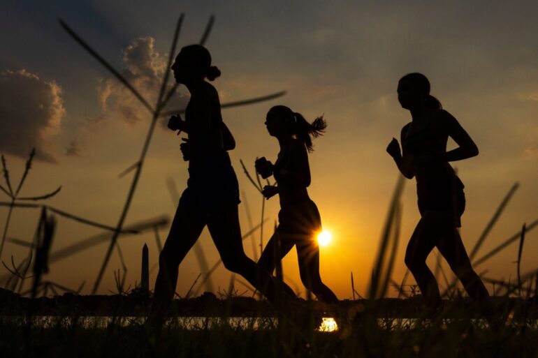 Menschen joggen am Potomac River entlang, während die Sonne in der Nähe des Washington Monument aufgeht.