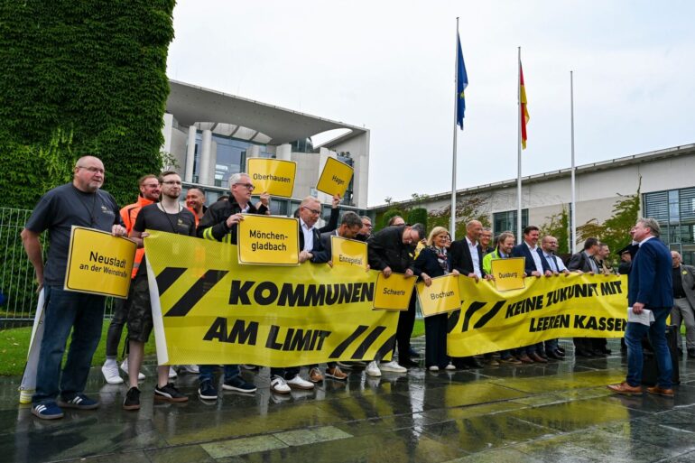 Vertreter mehrerer Städte und Kommunen demonstrieren mit Schildern und Bannern für finanzielle Unterstützung in Berlin.