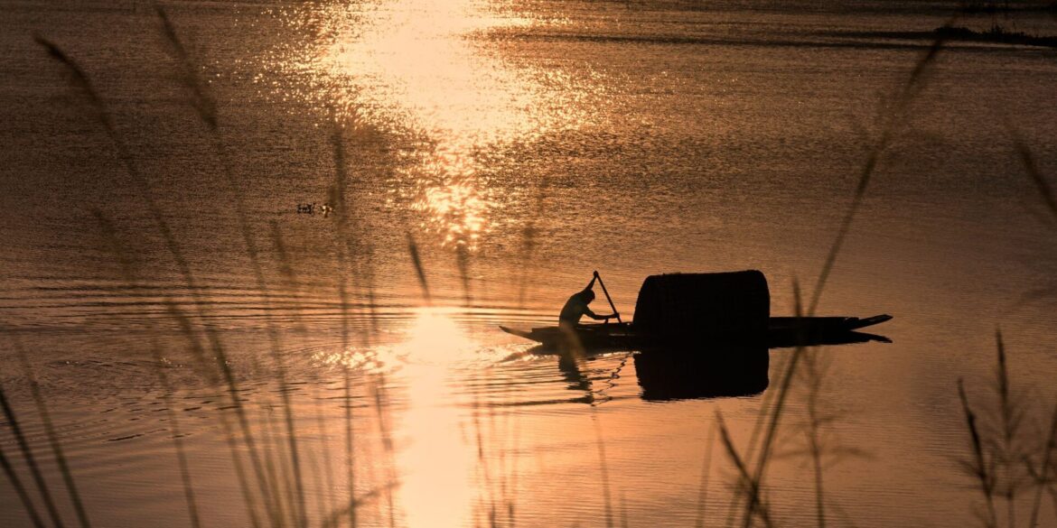 Ein Fischer rudert in einem Boot durch das steigende Wasser auf einem Reisfeld am Stadtrand von Guwahati, Indien.