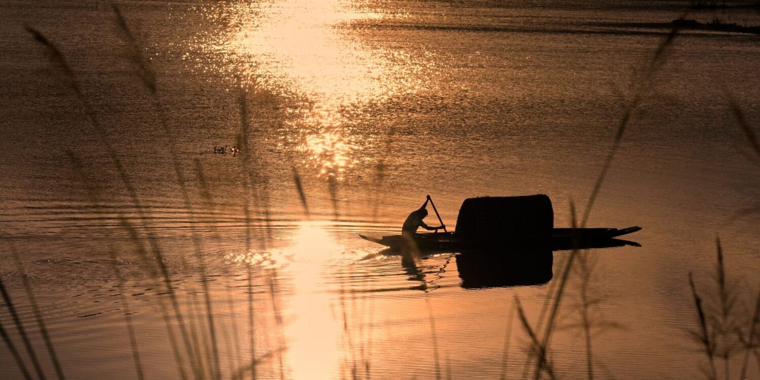 Ein Fischer rudert in einem Boot durch das steigende Wasser auf einem Reisfeld am Stadtrand von Guwahati, Indien.