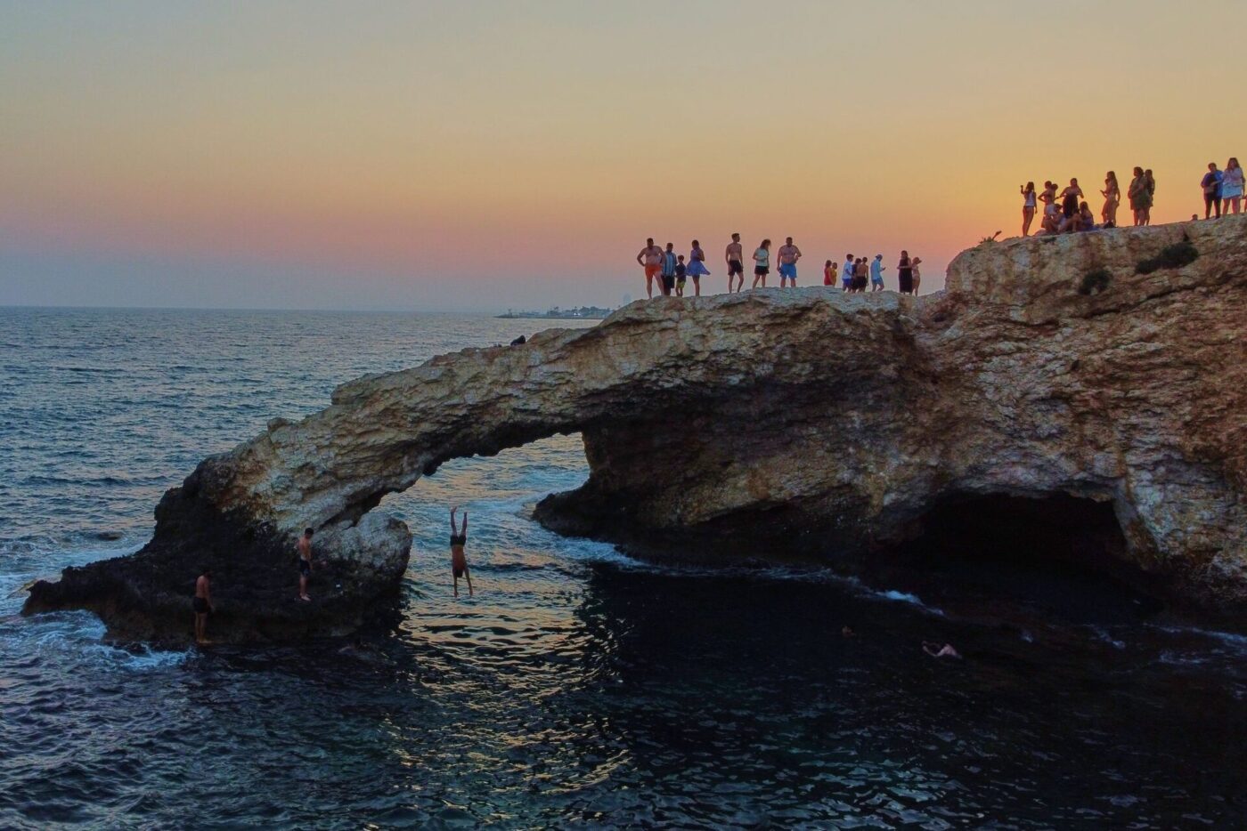Ein junger Mann springt bei Sonnenuntergang im Ferienort Ayia Napa auf der im östlichen Mittelmeer gelegenen Insel Zypern von der natürlichen "Liebesbrücke" ins Meer.