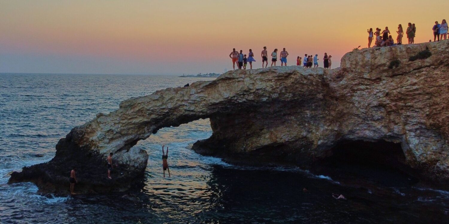 Ein junger Mann springt bei Sonnenuntergang im Ferienort Ayia Napa auf der im östlichen Mittelmeer gelegenen Insel Zypern von der natürlichen "Liebesbrücke" ins Meer.