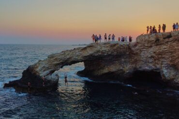 Ein junger Mann springt bei Sonnenuntergang im Ferienort Ayia Napa auf der im östlichen Mittelmeer gelegenen Insel Zypern von der natürlichen "Liebesbrücke" ins Meer.