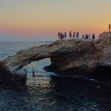 Ein junger Mann springt bei Sonnenuntergang im Ferienort Ayia Napa auf der im östlichen Mittelmeer gelegenen Insel Zypern von der natürlichen "Liebesbrücke" ins Meer.