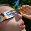 Eine junge Frau schaut durch eine Sonnenfinsternisbrille und betrachtet die Mittagssonne.