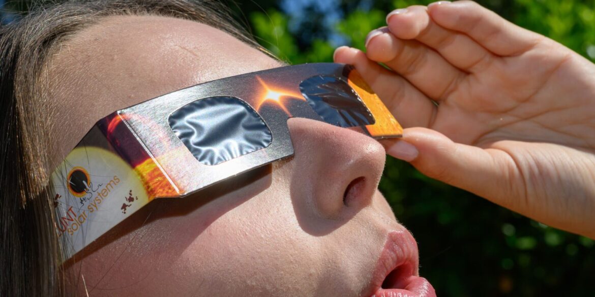 Eine junge Frau schaut durch eine Sonnenfinsternisbrille und betrachtet die Mittagssonne.