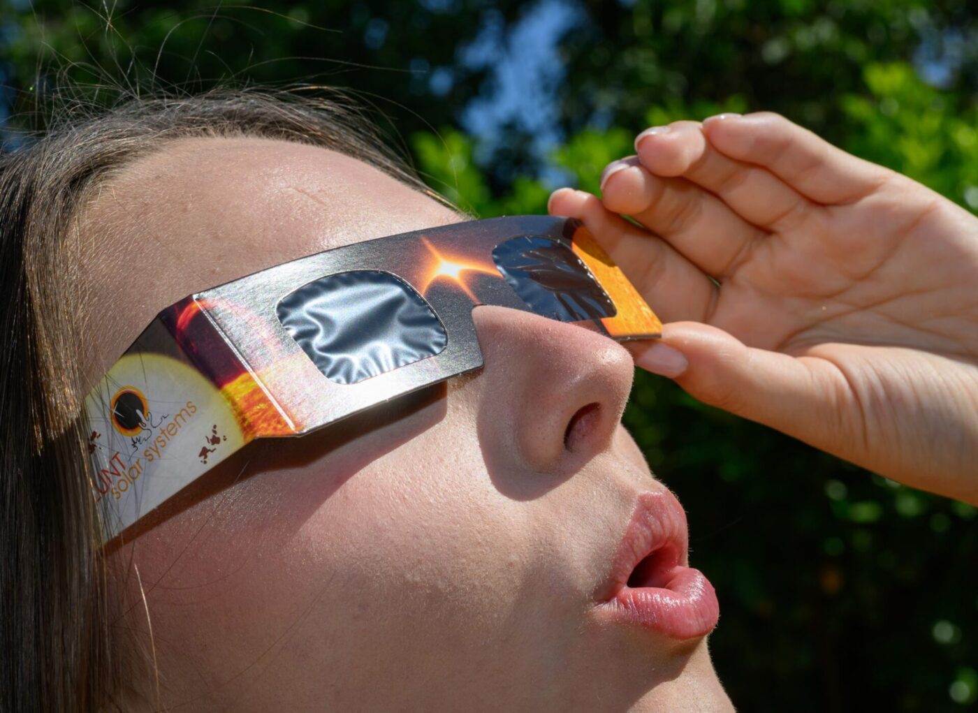 Eine junge Frau schaut durch eine Sonnenfinsternisbrille und betrachtet die Mittagssonne.