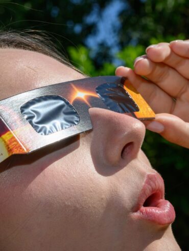 Eine junge Frau schaut durch eine Sonnenfinsternisbrille und betrachtet die Mittagssonne.