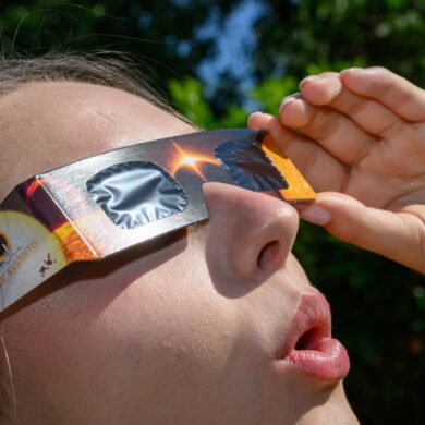 Eine junge Frau schaut durch eine Sonnenfinsternisbrille und betrachtet die Mittagssonne.