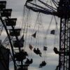 Wiesn-Besucher sitzen am Abend in einem Karussell vor dem Riesenrad auf dem Oktoberfest.