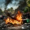 Demonstranten stehen bei Protesten um brennende Mülltonnen.