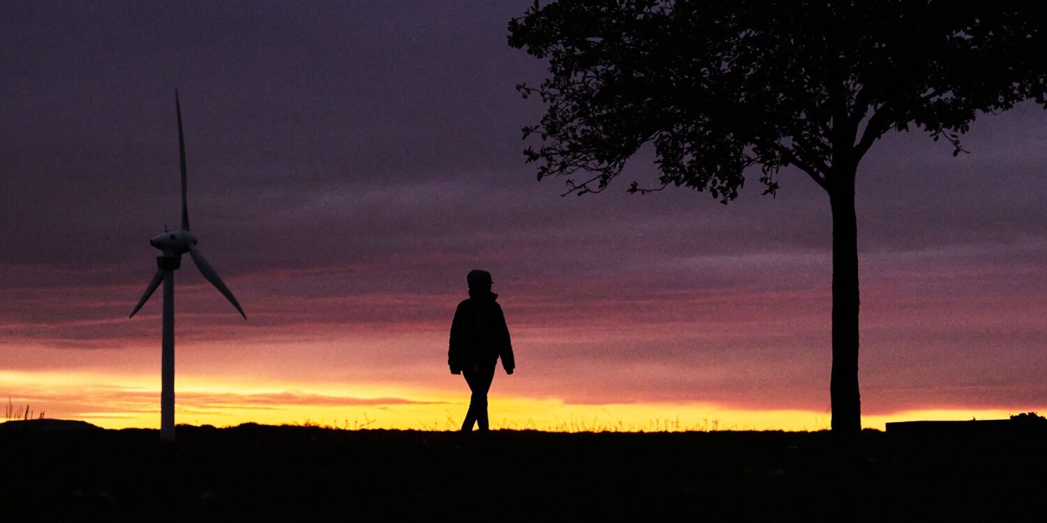 Eine Frau spaziert vor der vom Sonnenaufgang verfärbten morgendlichen Wolkenkulisse bei Hannover.