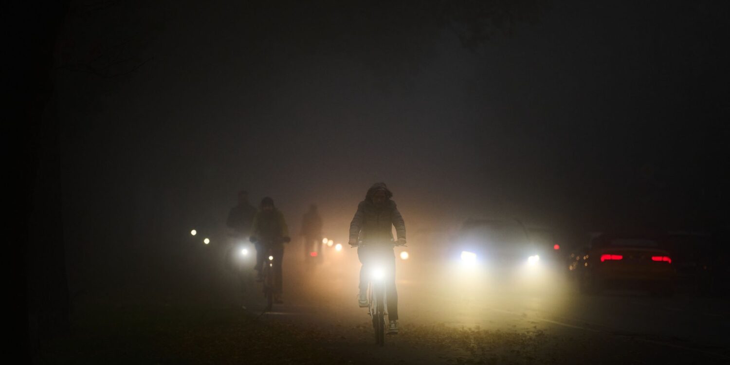 Rad- und Autofahrer fahren am frühen Morgen im Nebel über den Osterdeich.
