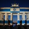 Teilnehmer stehen vor dem mit der Fahne Israels angestrahlten Brandenburger Tor und gedenken bei der Veranstaltung zum Jahrestag des Terrorangriffs der Hamas auf Israel am 7. Oktober 2023 den Opfern.