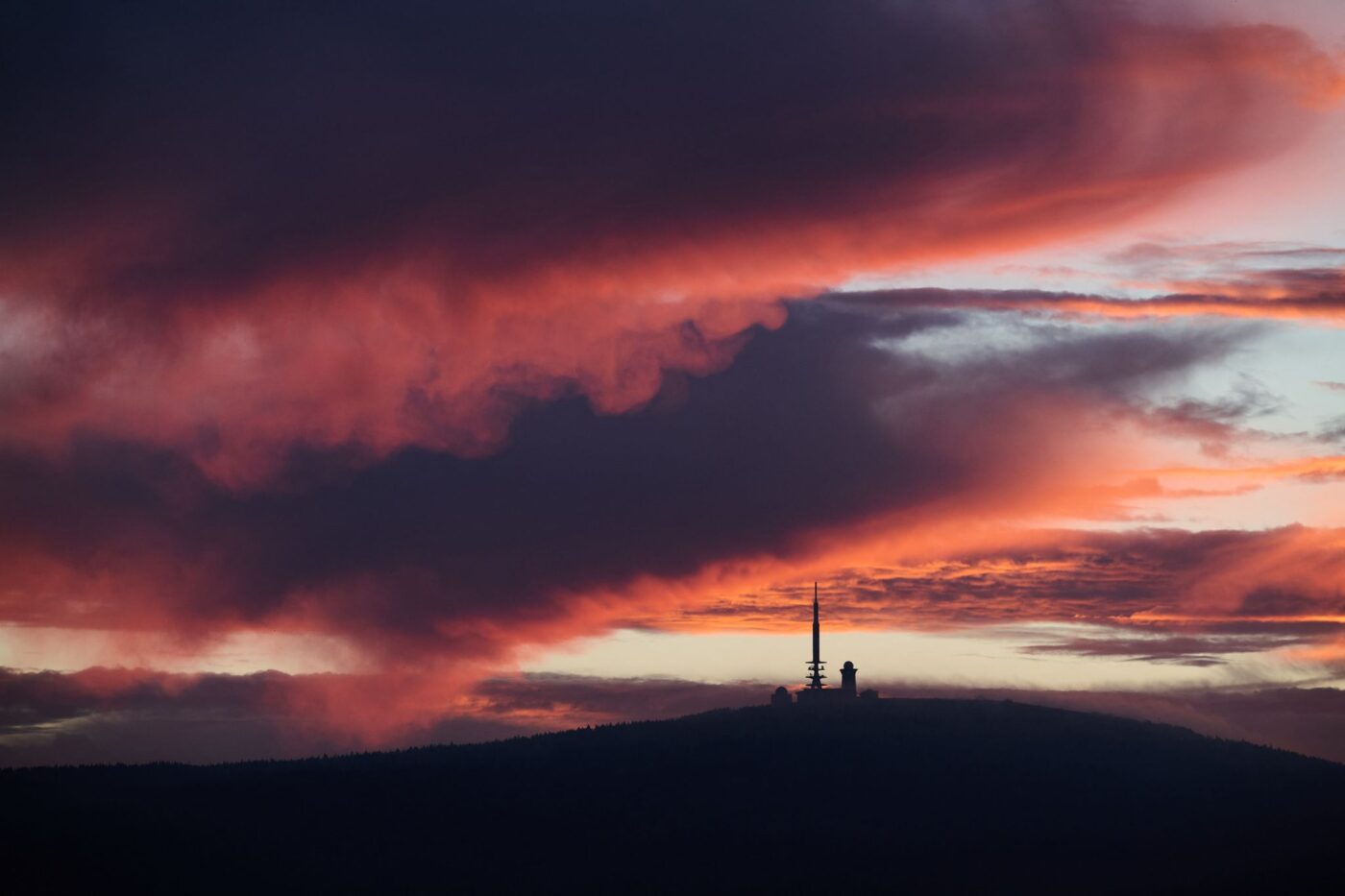 Vom Sonnenaufgang rötlich verfärbt zeigt sich der Himmel über dem Brocken in Sachsen-Anhalt.
